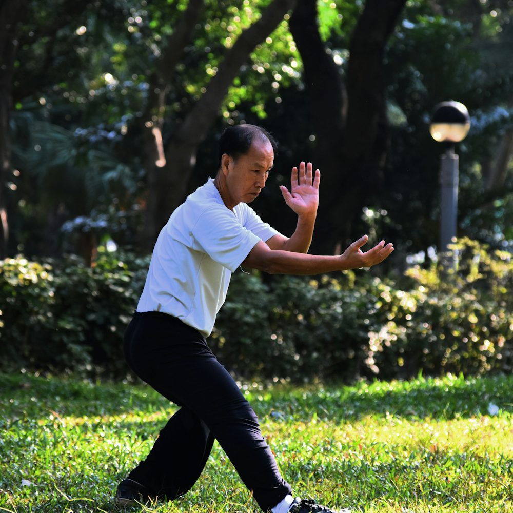 An older man practising tai chi among trees