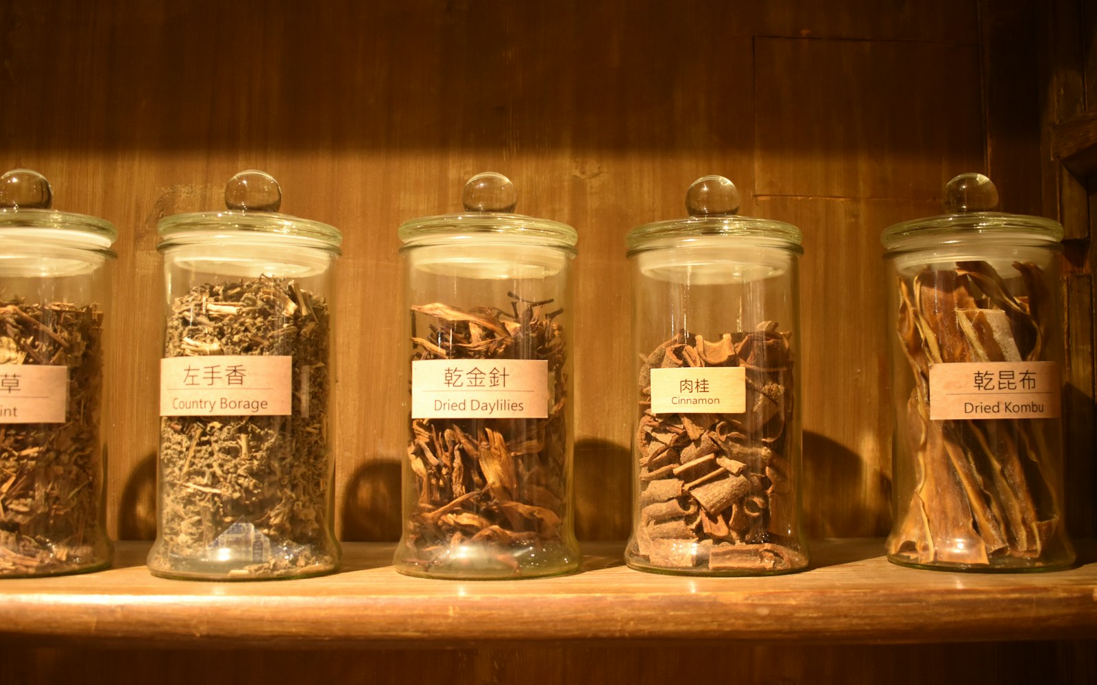 Glass jars of dried herbs on a wooden shelf